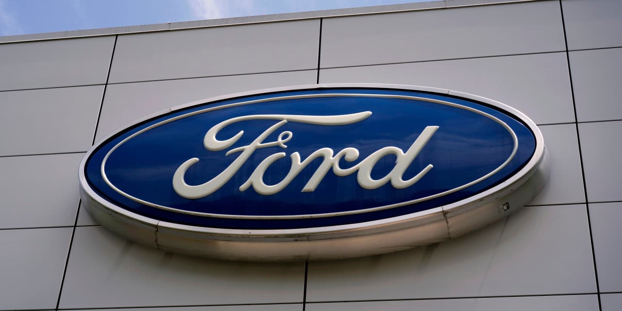 The Ford logo, an oval with the name "Ford" in script, is affixed to a building under a blue sky. (via wsj.com)