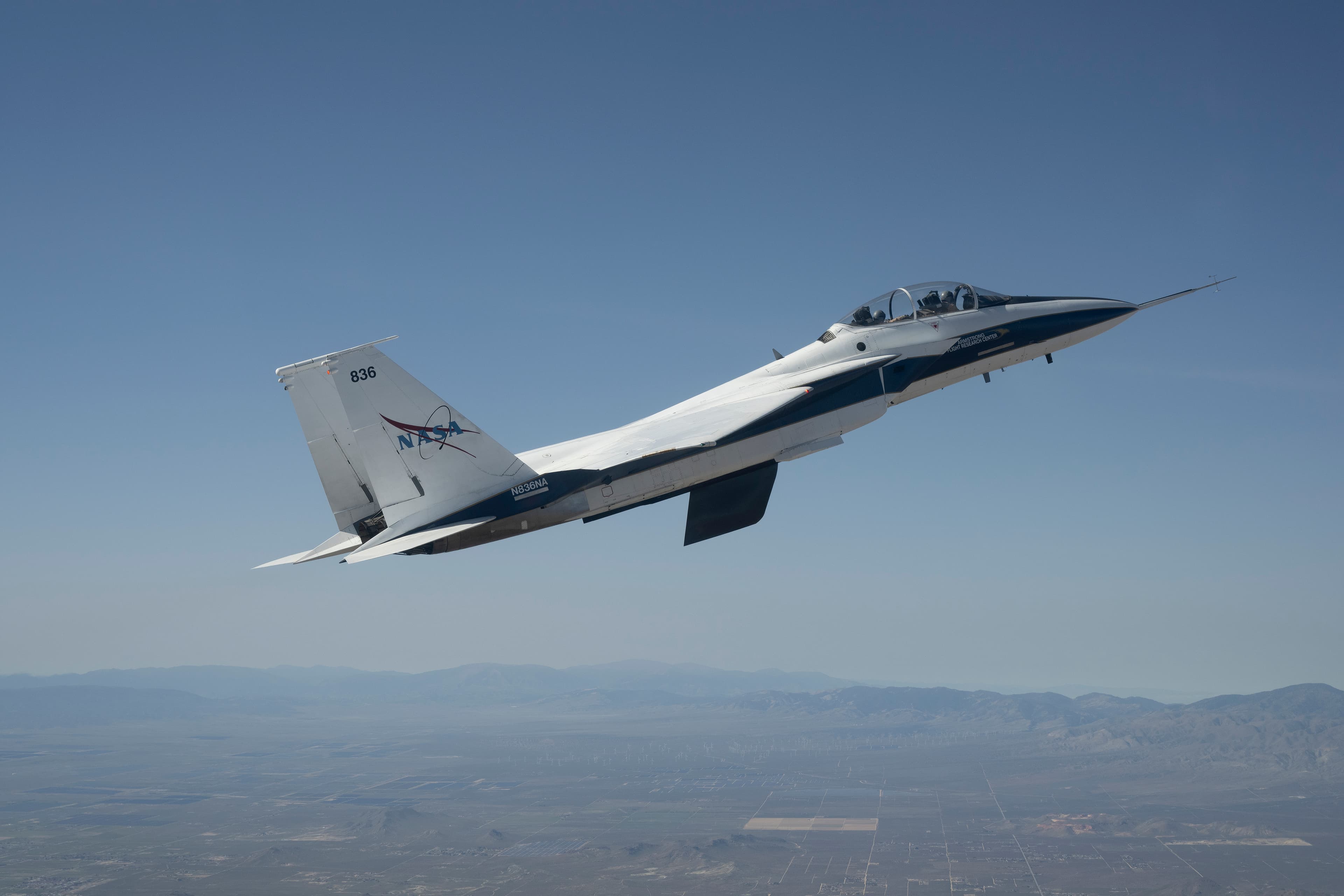NASA F-15 research jet in flight with experimental CATNLF wing model mounted beneath its fuselage against a blue sky