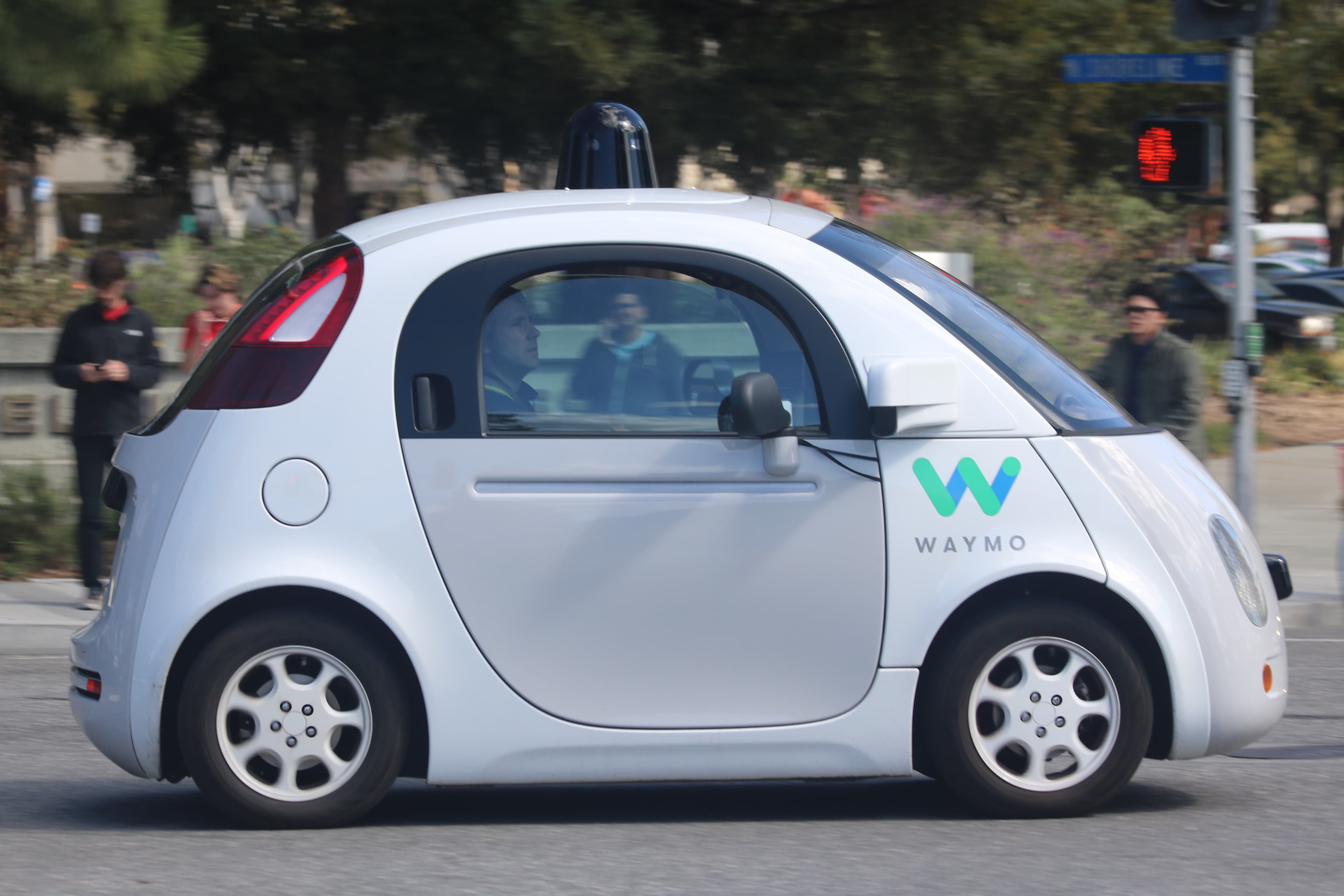 White Waymo self-driving car with rooftop lidar sensors viewed from the side